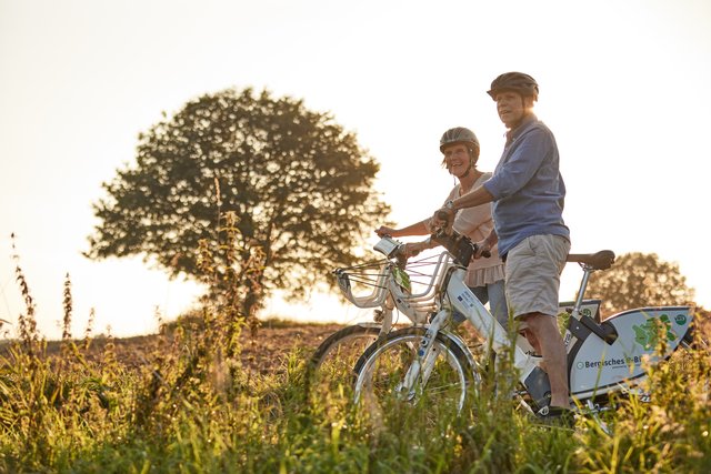 Ein Mann und eine Frau stehen mit Bergischen e-Bikes beim Sonnenuntergang auf einem Feld.
